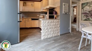 Een moderne keuken met houten kastjes, een vast eiland en een eethoek met een witte tafel en stoelen.