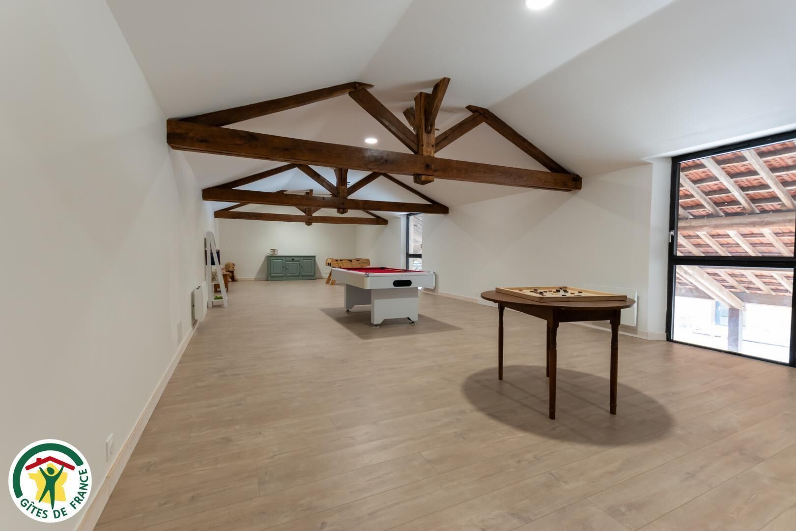 A spacious room with wooden beams on the ceiling, a pool table, and a foosball table.