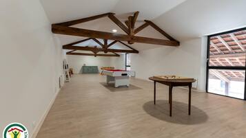A spacious room with wooden beams on the ceiling, a pool table, and a foosball table.