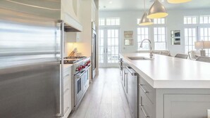 Une cuisine moderne dotée d’appareils électroménagers en acier inoxydable, d’un grand îlot central et de luminaires suspendus.