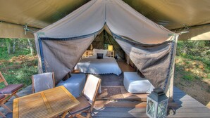 A tented accommodation with a bed, seating area, and a lantern.