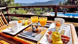 A breakfast tray with eggs benedict, orange juice, and ham on a wooden table overlooking a pool and mountains.