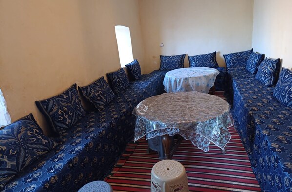 A room with a sofa set, a round table with a lace tablecloth, and a striped carpet. - Chez Mohamed Bennouri (Telouet)