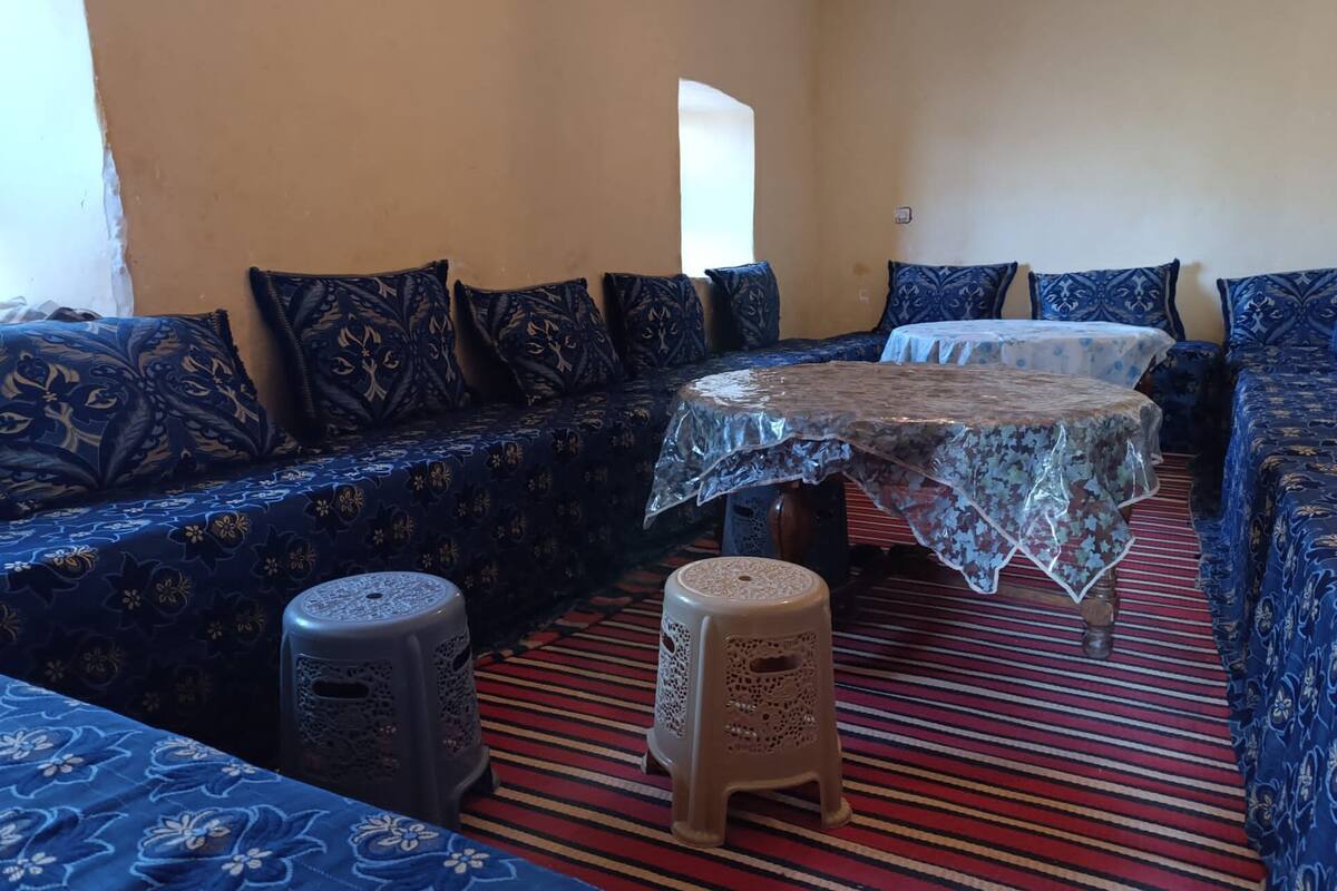 A room with a patterned blue sofa set, a small table with a lace tablecloth, and a striped carpet.