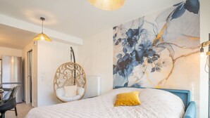 Un dormitorio con una cama grande, una silla colgante, un comedor con mesa y sillas, y una gran obra de arte floral en la pared.