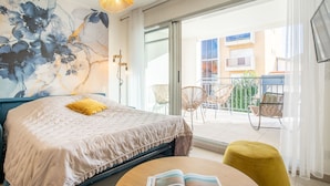 Un dormitorio moderno con una cama grande, un balcón con sillas de mimbre y vistas a la ciudad.
