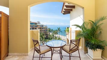 Un balcone con un tavolo rotondo e sedie, vista su una spiaggia e un complesso di edifici.