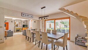 Un comedor amplio con una mesa grande y sillas, una chimenea y vistas al exterior a través de amplios ventanales.