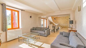 Amplia sala de estar con un sofá moderno, una mesa de centro de vidrio y un comedor con una escalera que conduce a un nivel superior.