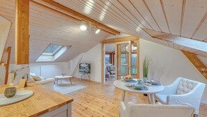 Um amplo loft com pé direito alto, vigas de madeira, claraboia, área de jantar com mesa redonda e um aconchegante espaço de estar.
