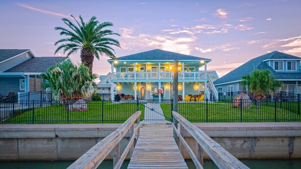 A waterfront property with a wooden dock leading to a two-story house with a balcony. - Copano Bay, Rockport, Tx. Waterfront, Private Pool & Hot Tub, & Pier  (Rockport)