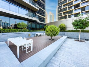 An outdoor patio area with a white table and chairs, surrounded by a low brick wall and a tree.