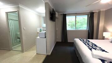 A hotel room with a bed, a small desk, a window with curtains, and a bathroom visible through an open door.