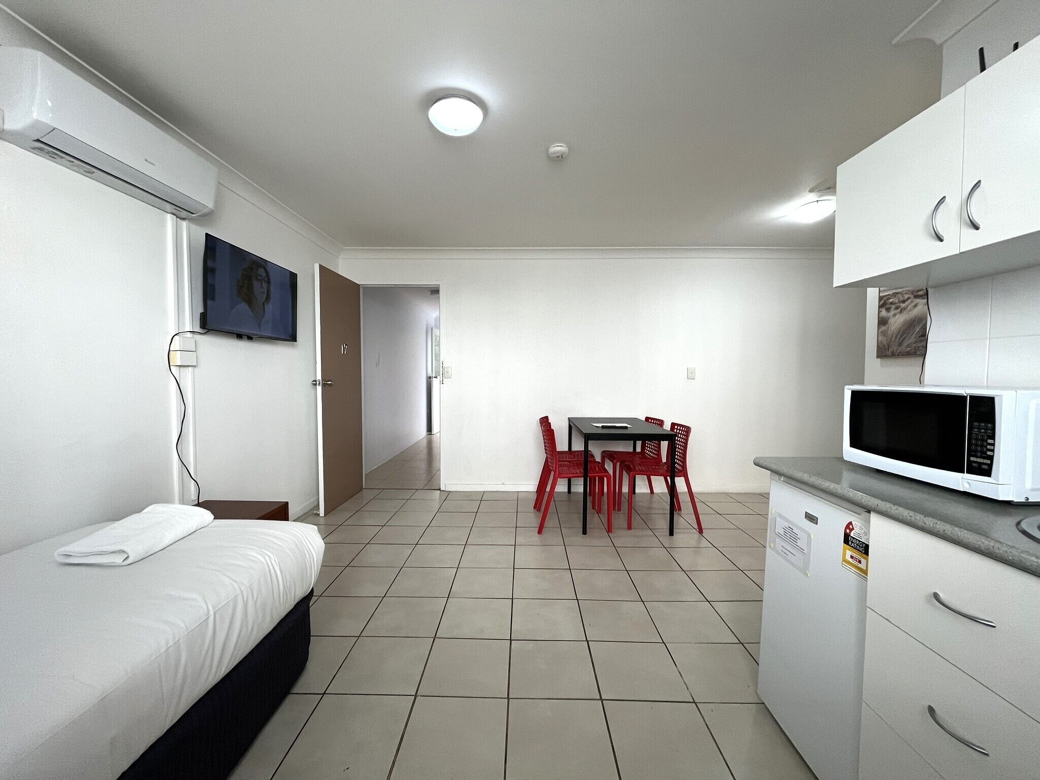 Una habitación pequeña y limpia con cama, una mesa con sillas, microondas y televisión.