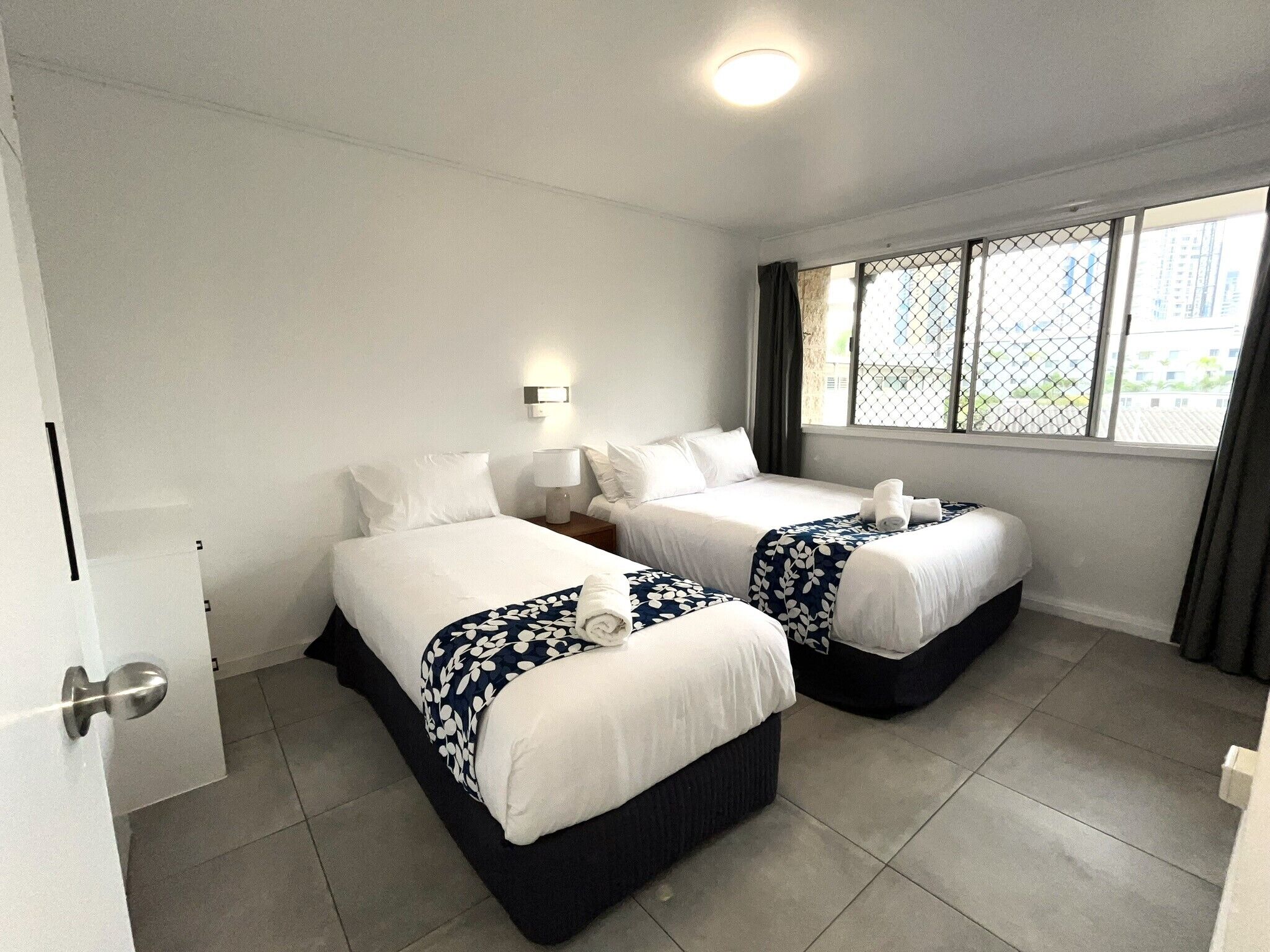 Une chambre d’hôtel avec deux lits, une table de chevet avec une lampe, une fenêtre donnant sur un paysage agréable et une porte.