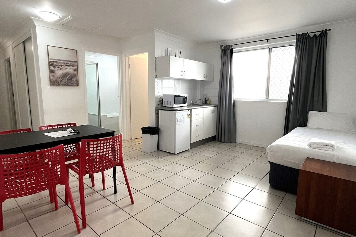 Una habitación de hotel compacta con comedor, kitchenette y cama.