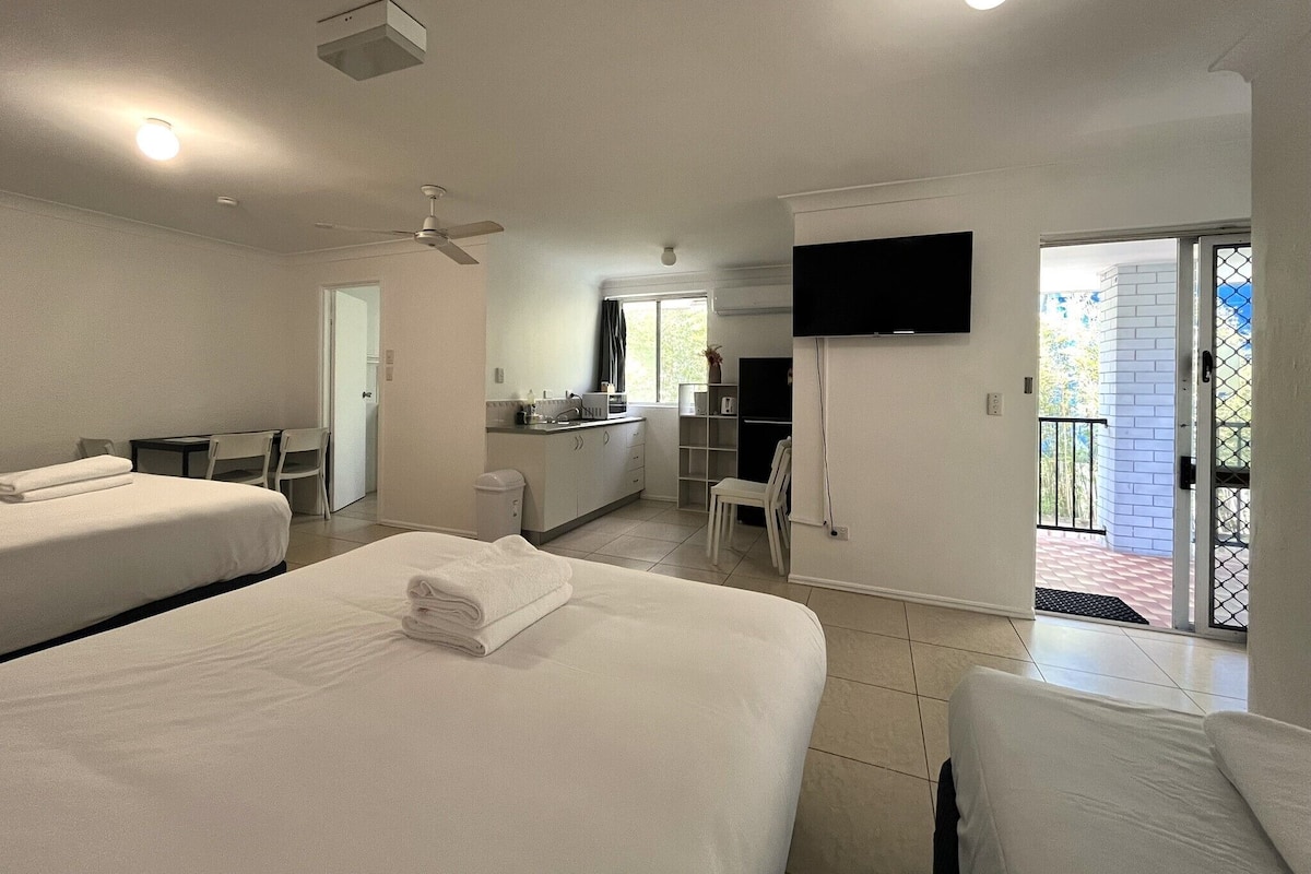 Habitación de hotel con dos camas, televisión, kitchenette y balcón.