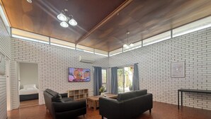 A spacious living room with a wooden floor, a TV mounted on the wall, and a bed visible through an open door. - Browns Broadbeach (Mermaid Beach)