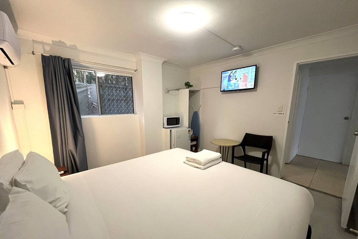 Una habitación de hotel con una cama, un televisor en la pared, una mesita pequeña y una silla.