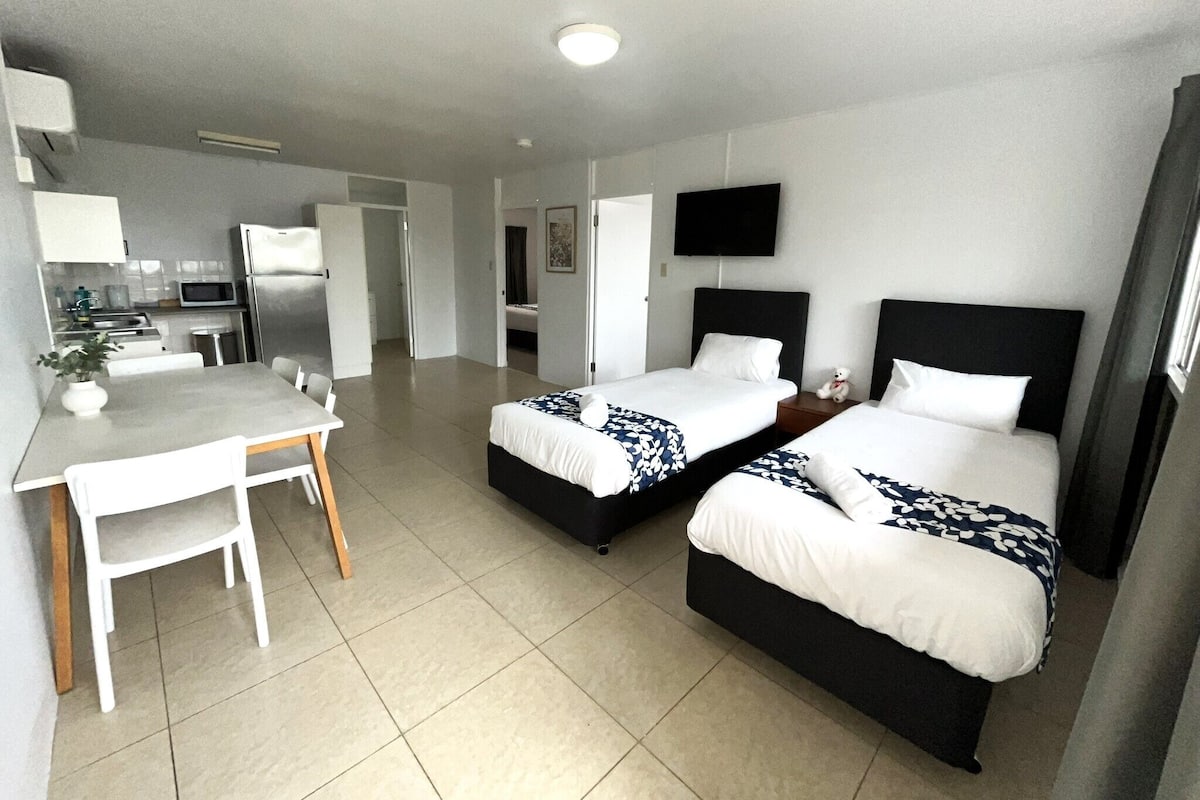 Habitación de hotel con dos camas, un escritorio y una kitchenette.