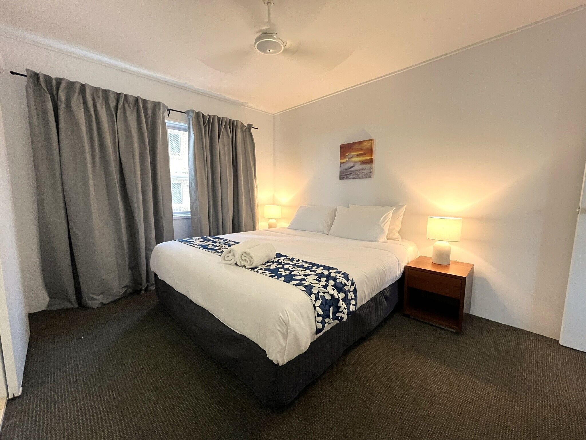 Una habitación de hotel con cama, dos lámparas de noche, una mesita de noche y una ventana con cortinas.