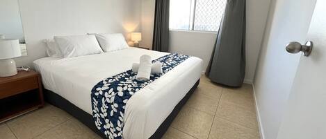 Une chambre d’hôtel avec un lit bien fait, une lampe de chevet, une fenêtre avec des rideaux et une porte dotée d’une poignée.
