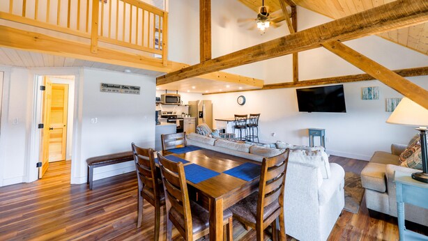 A spacious living area with a wooden dining table, high ceilings with exposed beams, a kitchen area, and a balcony. - Historic Barn Suites (Greenville)