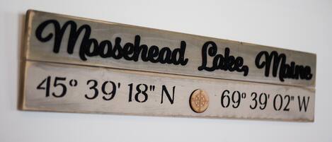 A metal sign with the text "Moosehead Lake, Maine" and coordinates "45° 39' 18" N, 69° 39' 02" W".