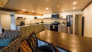 A modern kitchen with wooden ceiling, stainless steel appliances, and a dining area with a patterned chair. - Historic Barn Suites (Greenville)