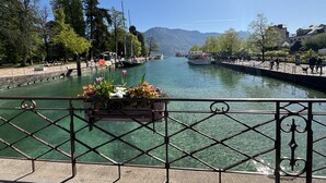 A river with boats, a bridge, and a railing with flowers. - View Point Impérial Lake 4* - OG IMMO (Annecy)