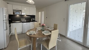 A modern kitchen with white cabinets, a microwave, and a dining area with a wooden table set for four. - View Point Impérial Lake 4* - OG IMMO (Annecy)