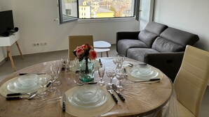 A dining area with a table set for four, a sofa, and a TV stand. - View Point Impérial Lake 4* - OG IMMO (Annecy)