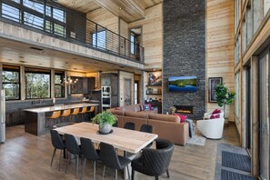 A spacious living area with a large wooden dining table, black upholstered chairs, a brown leather sofa, and a white armchair.