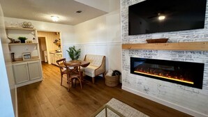 A living room with a fireplace, a television mounted on a brick wall, and a dining area with wooden furniture. - Southern Travel - Charming 3 BR (Moultrie)