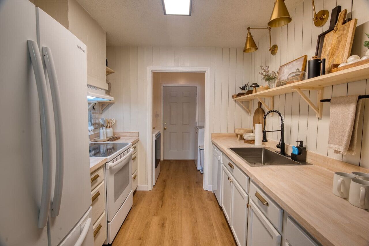 A kitchen with white cabinets, a wooden countertop, a sink, and a refrigerator.