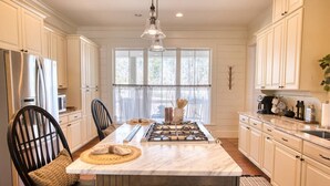 A kitchen with a central island, white cabinetry, a stainless steel refrigerator, and a hanging light fixture. - Southern Farmhouse Retreat: 4 Bedroom, 4 Bath w/Master SPA like - Pet Friendly (Moultrie)
