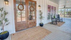 A covered porch with a wooden door, two potted plants, and a seating area with chairs. - Southern Farmhouse Retreat: 4 Bedroom, 4 Bath w/Master SPA like - Pet Friendly (Moultrie)