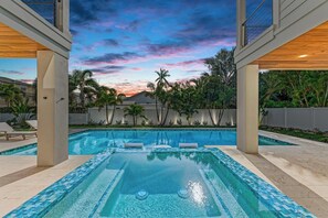 Piscina com vista para o pôr do sol, cercada por palmeiras e um muro.