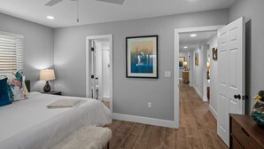 Un dormitorio con cama, un banco blanco, un ventilador de techo y un pasillo que conduce a otras habitaciones.