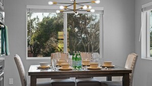 Un comedor con una mesa dispuesta para cuatro personas, una araña y un ventanal con vistas a árboles.