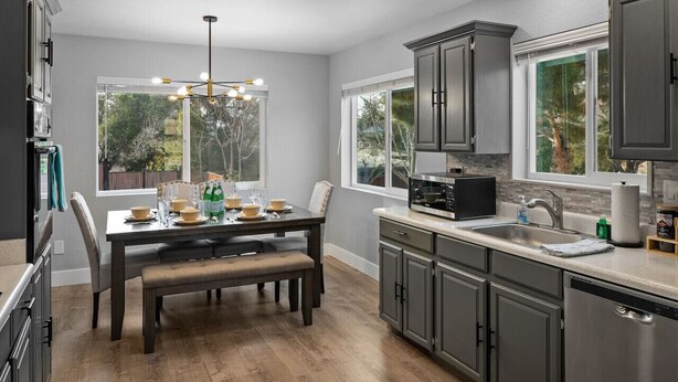 Una cocina moderna con armarios oscuros, una mesa de comedor preparada para cuatro personas y un amplio ventanal con vistas al exterior.