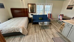 A bedroom with a bed, a blue sofa, a small table, a chair, and a kitchenette. - Wimble Shoals Chateau - Studio in Salvo above Surf Shop- (Salvo)