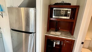 A compact kitchen with a stainless steel refrigerator, a microwave, and a sink under a wooden cabinet. - Wimble Shoals Chateau - Studio in Salvo above Surf Shop- (Salvo)