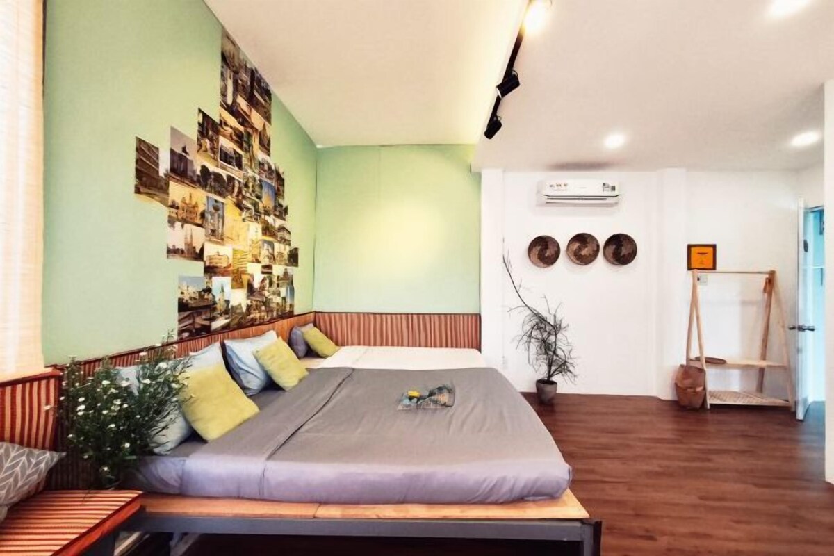 Un dormitorio con una cama, una pared con fotografías, una planta y suelo de madera.