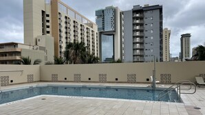 A rooftop pool area with tiled flooring and a pool, surrounded by high-rise buildings. - Free parking, chocolate covered MACO nuts/waters, F/Kitchen, GYM, AC, WiFi, pool (Honolulu)