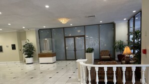 A spacious lobby with a tiled floor, a reception desk, a model building display, and a seating area with a lamp and plants. - Free parking, chocolate covered MACO nuts/waters, F/Kitchen, GYM, AC, WiFi, pool (Honolulu)