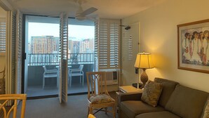 A hotel room with a balcony, a sofa, a chair, a table, and a lamp. - Free parking, chocolate covered MACO nuts/waters, F/Kitchen, GYM, AC, WiFi, pool (Honolulu)