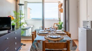 Een eetgedeelte met een tafel voor vier personen, een televisie op een dressoir en uitzicht op zee door een schuifdeur.