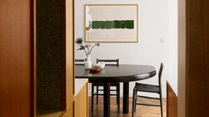 Un comedor con una mesa redonda, sillas, un florero con flores y un cuadro abstracto enmarcado en la pared.