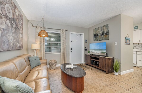 Un salon avec un canapé en cuir, une table basse, un téléviseur et un tableau accroché au mur.